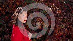 Close-up of girl in a red coat walking in autumn park with colored autumn leaves