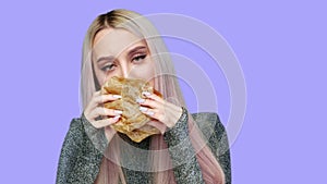 Close-up of a girl with red lipstick on her lips, eating a hamburger on a purple background. Diet. The concept of