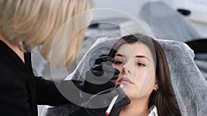 Close-up of a girl's face during lip makeup. A beautician applies permanent lip color