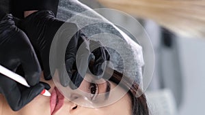 Close-up of a girl's face during lip makeup. A beautician applies permanent lip color. Vertical