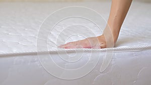 Close up of a girl's hand checks the rigidity of a new comfortable orthopedic white mattress for the bed. Female