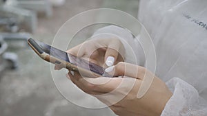 Close-up of a girl's hand in a disposable overalls using a smartphone for messages. Slow motion video.