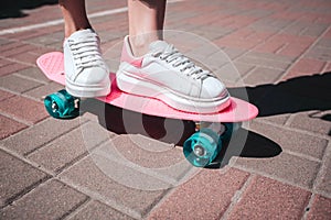 Close up of girl`s legs and feet wears white sneakers. Girl is standin on pink skate with both feet. There is a sunny