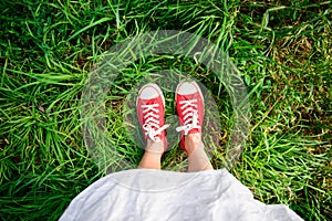 Close up of girl's legs in red keds on grass.