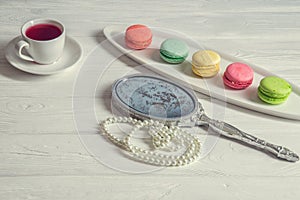 Close up. Girl`s morning. Bright colorful macarons, a cup of berry tea, a pocket mirror, a pearl thread. White background