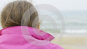 Close-up of a girl sitting on the seashore from the back