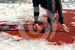 Close-up girl in sportswear on the track for running on a snow-covered stadium is preparing to jog. running from a low start to a