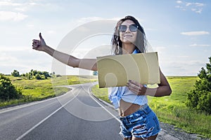 Close up girl travels hitchhiking with a cardboard sign in her hands. a girl in glasses shorts and heels road on