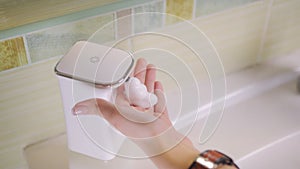 Close-up of a girl using an automatic soap dispenser in the bathroom.