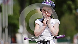 Close-up of the girl wearing helmet and then rides a bicycle in the city park.