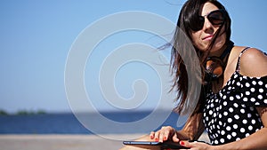 Close-up, girl works on a tablet, female hands, legs with bright red manicure, nails, pedicure, on the beach, on a hot