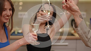 Close-up. The girls are holding tall and thin glasses on a long stem with white sparkling wine in their hands. Amid