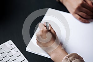 Close-up of a girls left-handed girls hand who writes on white sheets while sitting at a table in an office or library