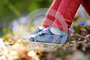 Close-up of girls shoes in the woods on beautiful sunny spring day. Child picking the first flowers of spring outdoors