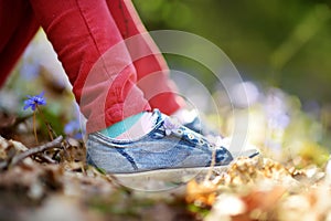 Close-up of girls shoes in the woods on beautiful sunny spring day. Child picking the first flowers of spring outdoors