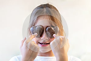 Close up glad joyful laughing child closing eyes by two cookies pastry in shape of heart in her hands, indulges. Concept