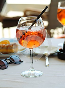 Close up of a glass of aperol spritz or campari orange cocktail with orange slice and ice on a restaurant table on the seashore on