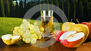 Close-up of a glass of apple juice, apples and grapes on a wooden table.