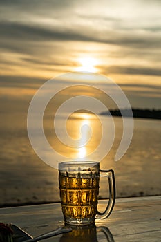 Close up a Glass of beer is standing on a table with blurred sea on background. Beer with foam. Sunset and natural. Alcohol and