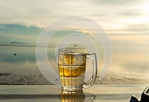 Close up a Glass of beer is standing on a table with blurred sea on background. Beer with foam. Sunset and natural. Alcohol and