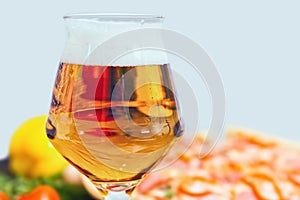 Close up of glass of beer and tasty pizza with salami on background