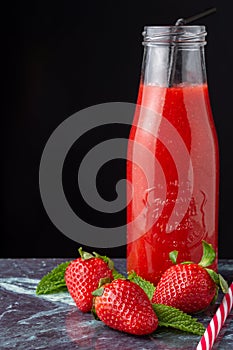 Close-up of glass bottle with strawberry juice, black and striped straw, with strawberries, on blue marble and black background, v