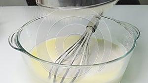 close-up of a glass bowl with liquid dough slow motion, the girl adds flour sifted through a metal sieve into the