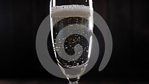 Close-up of a glass of champagne with bubbles on a black background, slow motion