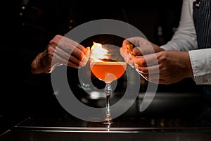 close-up of glass with cocktail on which the splashes and set on fire hands of bartenders