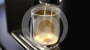 Close-up. A glass coffee cup is filling up with fresh coffee from a coffee machine.