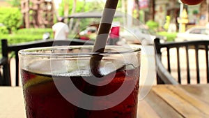 Close up of a glass of cola-colored fizzy drink with Asian tuk tuks passing i