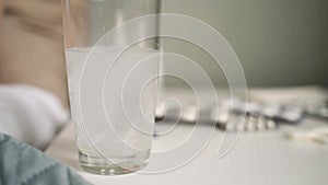 Close-up of a glass with a dissolving tablet on a bedside table. In the background a sick girl waiting in bed