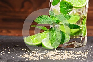 Close-up of a glass full of an alcoholic mojito from sour lime, rum, mint and ice cubes on a dark wooden background.