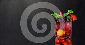 close up of a glass full of colorful fruits and berries and mint served with ice and soda as summer refreshment