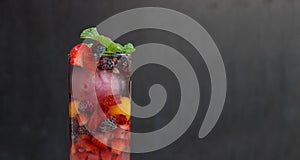 close up of a glass full of colorful fruits and berries and mint served with ice and soda as summer refreshment