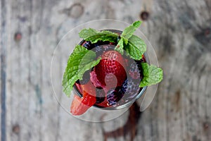 close up of a glass full of colorful fruits and berries and mint served with ice and soda as summer refreshment