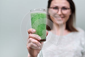 Close up glass with green natural vegetable smoothie drink in woman`s hand