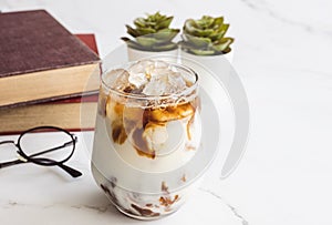 Close up a glass of iced coffee latte with glasses and the book on white background, cool drama  tone image for relaxing, feeling