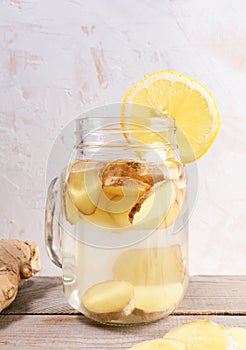 Close-up glass jar with ginger water and lemon slice on wooden table.