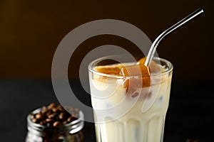 Close-up glass with milk and ice cubes made from coffee. Iced coffee with a metal tube on a brown background.