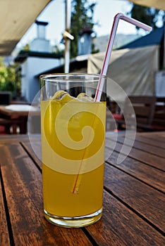 A close up of a glass of orange juice and ice cubes with a straw bent over the glass