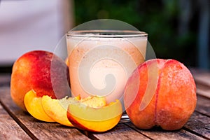 Glass of peach yoghurt and peaches on wooden table