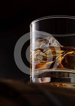 Close up of glass of single malt whiskey with ice cubaes on top of wooden barrel on black