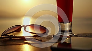 Close up of glass of tequila sunrise alcoholic cocktail standing on the wooden table next to the sunglasses and mobile