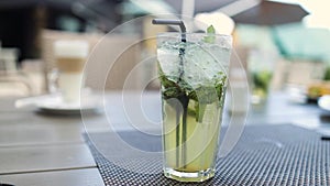 Close up of glass with tropical mojito cocktail fresh green mint and lime ice cube on light table background with copy