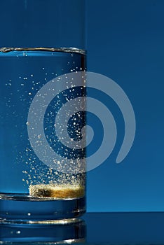Close up of glass of water with effervescent aspirin tablet, pill in it isolated over blue background. Health concept