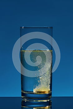 Close up of glass of water with effervescent aspirin tablet, pill in it isolated over blue background. Health concept