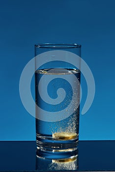 Close up of glass of water with effervescent aspirin tablet, pill in it isolated over blue background. Health concept