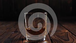 Close-up of a glass of whiskey on a dark wooden surface.