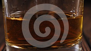 Close-up of a glass of whiskey on a dark wooden surface.